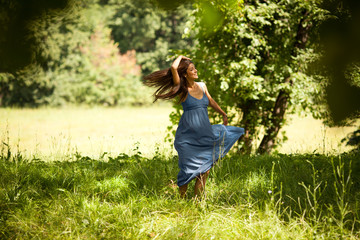 Naklejka na ściany i meble Attractive female model in blue dress.She walking trough meadow.