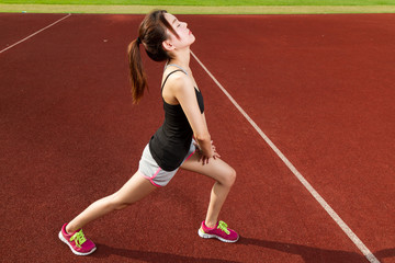 Fototapeta na wymiar Chinese female athelete stretching legs on sports field, warming