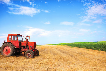 old red tractor during wheat harvest on cloudy summer day