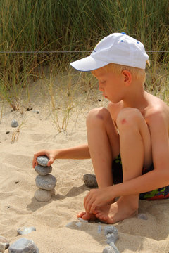 The boy builds the pebbles stack on the sand