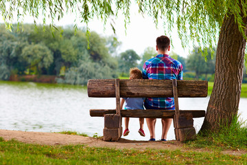 father and son sitting on the bench near the lake
