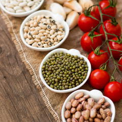 Legumes in bowls, tomatoes, garlic and olive oil on wooden table