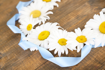 Obraz premium Chamomile wreath with blue ribbon on brown wooden background