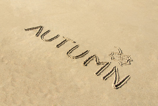Word autumn handwritten and leaf drawn in sand