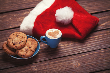 Obraz na płótnie Canvas Cookie and cup of coffee with santa's hat on wooden table.