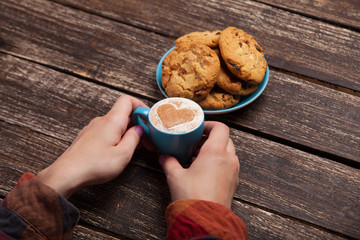 Female hands holding cup of coffee and cookies on wooden table.