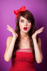 Surprised girl in red dress on violet background.