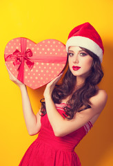 Beautiful brunette girl in christmas hat with gift on yellow bac