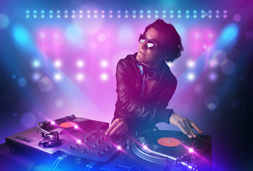 Disc jockey mixing music on turntables on stage with lights and