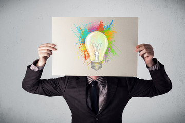 Businessman holding a cardboard with paint splashes and lightbul