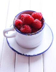 Ripe sweet raspberries in cup on table close-up