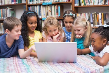 Fototapeta na wymiar Cute pupils looking at laptop in library