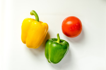 Paprika gelb gruen und Tomate nebeneinander auf weiss