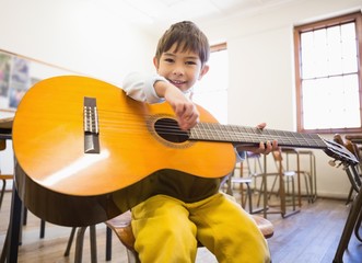 Cute pupil playing guitar in classroom - Powered by Adobe