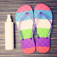 Flip flops and Bottle with suntan cream on wooden floor.