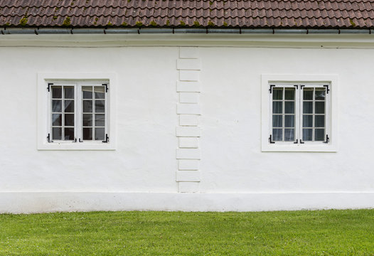 The old white plastered wall with a windows and green lawn befor