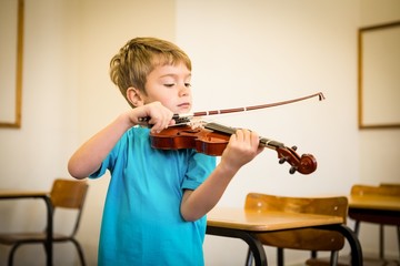 Cute pupil playing violin in classroom