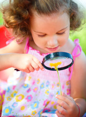 Young girl is looking at flower through magnifier