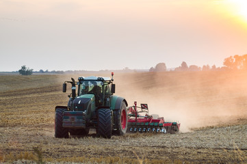 Traktor orzący pole podczas zachodu słońca
