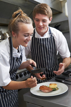 Chef Instructing Trainee In Restaurant Kitchen