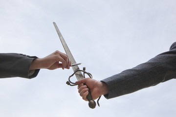 Arms of men in suits dueling with a pen and sword.