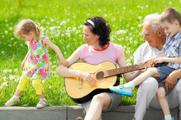 young happy mother playing guitar for her young children 