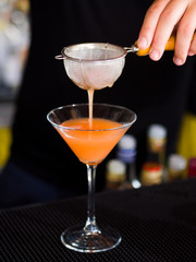Bartender pooring cocktail into Martini glass