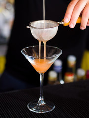 Bartender pooring cocktail into Martini glass