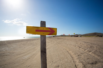 Wooden sign with an arrow and the beach in the backgound