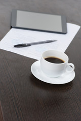 Tablet computer with cup of coffee and pen at table.