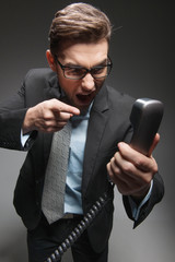 Angry businessman yelling into landline phone on white.