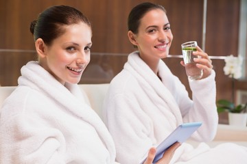 Women in bathrobes drinking water and text messaging