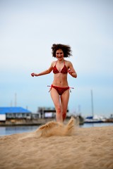 The young woman runs on a beach scattering feet sand