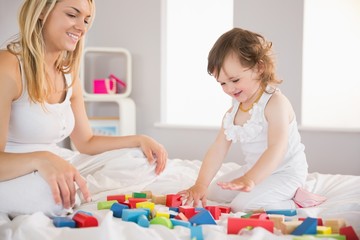 Mother and daughter playing with building blocks on bed