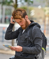Lost bearded male tourist holding a map and gesturing with hands