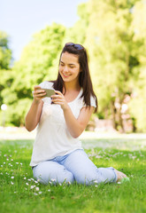 Obraz premium smiling young girl with smartphone sitting in park