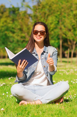 smiling young girl with book sitting on grass
