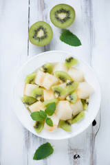 Salad with melon and kiwi on a wooden background, above view