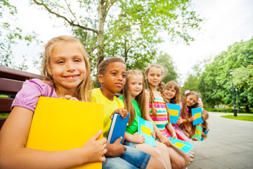 Kids sitting together on brown bench with books