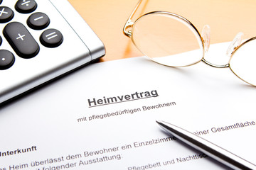Vertrag für Pflegeheim, Altersheim oder Seniorenheim mit Taschenrechner, Brille und Kuli.