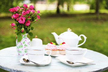 Coffee table with teacups and tasty cakes in garden