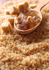 Reed sugar in wooden spoon on brown crystal sugar background