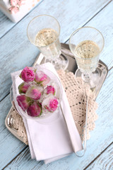 Ice cubes with rose flowers in glass bowl and two glasses with