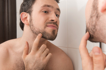Obraz premium Closeup of young man examining his stubble in mirror.