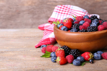 Ripe sweet different berries in bowl, on old wooden table