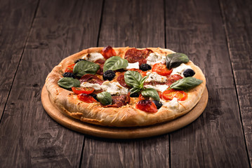 Pizza with salami, mozzarella, olives and basil on wooden table