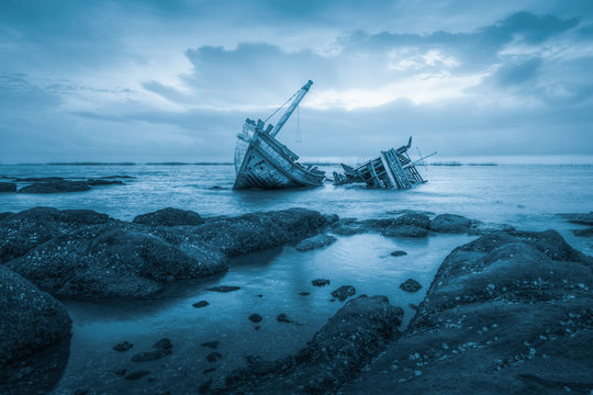 Fototapeta Shipwreck or wood ship broken damage on land, coast or beach with sea and sunset background. That result of accident, storm, crash, wave in ocean or marine. For assurance, travel or adventure concept.