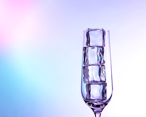 Glass with ice cubes on color background