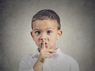 Boy placing finger on lips showing quiet gesture grey background