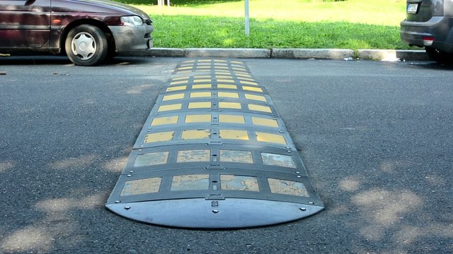 speed humps - car passing - parked cars with grass in background